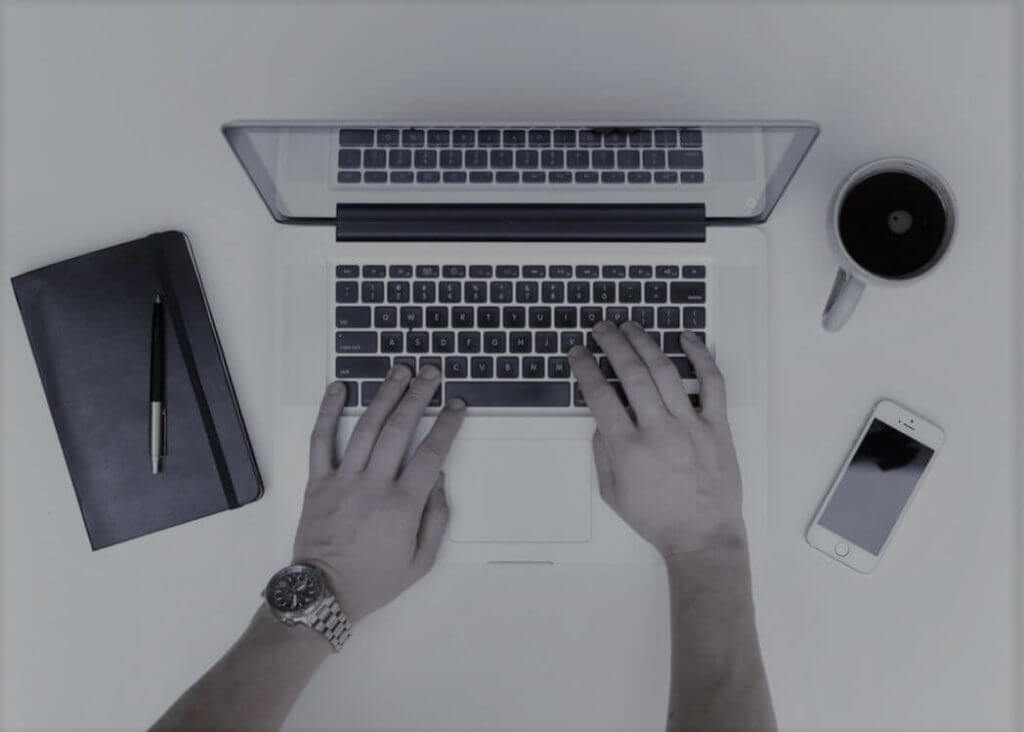 macbook med kaffekopp, anteckningsblock och iphone bredvid